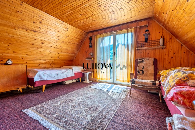 Rekreačná chata s krásnym pozemkom a potenciálom výstavby domu - Drevený obklad, koberce a posteľ v interiéri Chaty vytvárajú útulnú atmosféru.