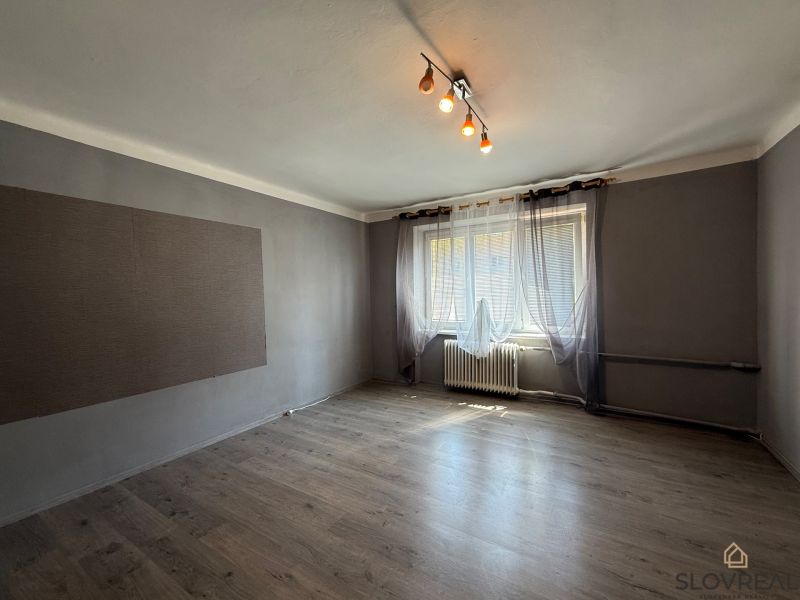 Na predaj 3 byt Žiar nad Hronom, 75m2 - Obývacia izba v 3-izbovom byte s podlahou s dreveným dekorom a veľkým oknom.