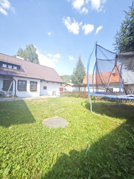 Predaj: Štýlová chalupa v srdci Španej Doliny miesto s atmosférou  - Chata v Španej Doline s trampolínou na trávnatej záhrade pod modrou oblohou.