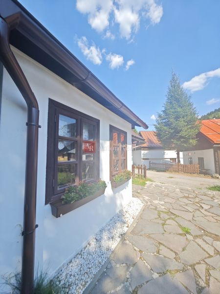 Predaj: Štýlová chalupa v srdci Španej Doliny miesto s atmosférou  - Chata v Španej Doline so záhonom pri okne a vydláždeným chodníkom.