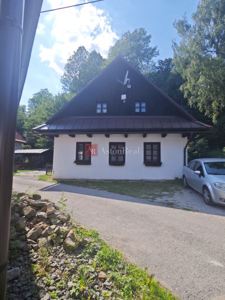 Predaj: Štýlová chalupa v srdci Španej Doliny miesto s atmosférou  - Chata v Španej Doline s bielou fasádou a satelitnou anténou, obklopená zeleňou.