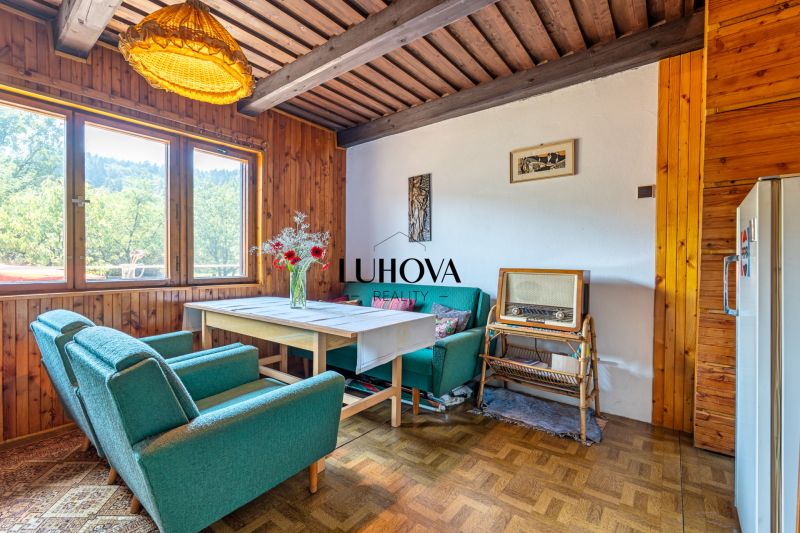 Rekreačná chata s krásnym pozemkom a potenciálom výstavby domu - Interiér chaty s retro nábytkom a podlahou s dreveným dekorom, pohodlné kreslá, vintage rádio.