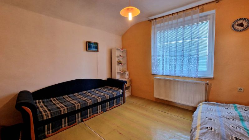 Na predaj dvojpodlažný rodinný dom v obci Kazimír, okres Trebišov - Obývačka v Rodinnom dome s pohovkou, poličkou a závesom za oknom.