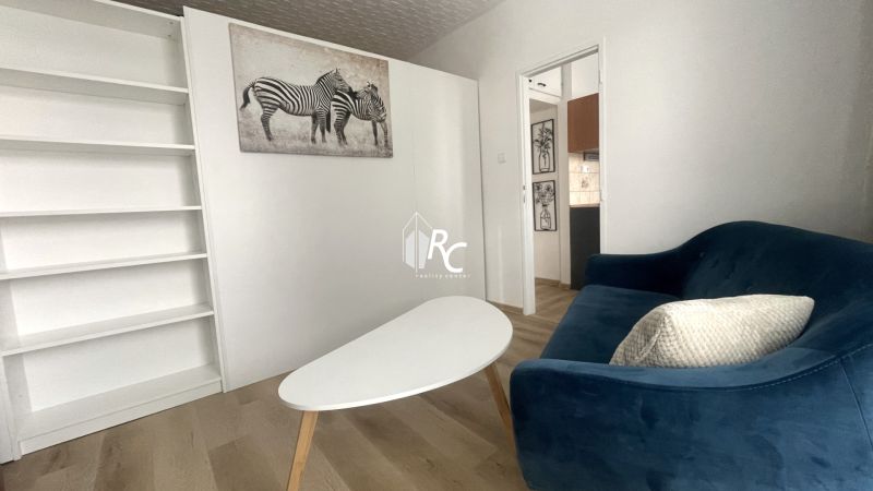 Prenájom 2-izbový byt s balkónom Martin – Podháj (41m2) - Obývačka so sedačkou a bielym stolíkom, podlaha s dreveným dekorom v 2-izbovom byte.