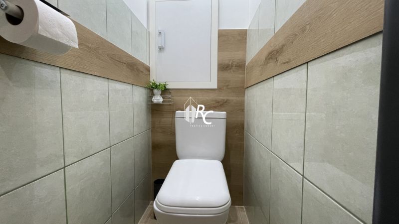 Prenájom 2-izbový byt s balkónom Martin – Podháj (41m2) - Toaleta s podlahou s dreveným dekorom v 2-izbovom byte, dekoratívna rastlina, polička.