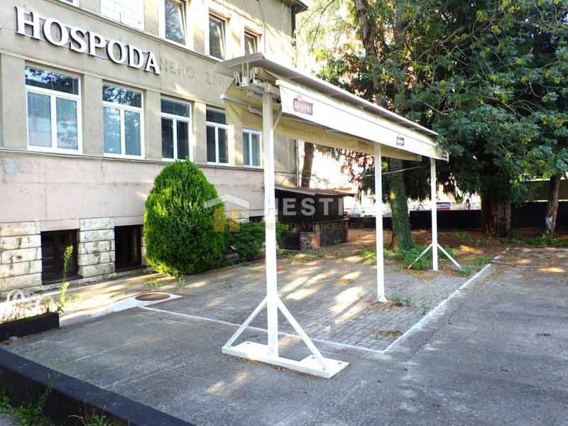Reštaurácia s terasou na prenájom – centrum mesta - Obchodné priestory v Senici s parkoviskom, zeleňou a nápisom na budove.