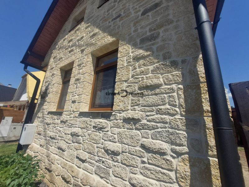 NA PREDAJ Čarovný vidiecky dom s kachľovou pecou NEMECKÁ - Kamenná fasáda rodinného domu v Nemeckej s dreveným dekorom na streche.