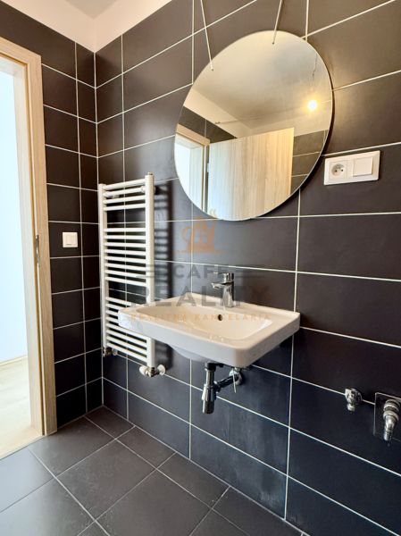 Na predaj novostavba 3 izbový byt, Bratislava, Nový Ružinov, Bajkalská - Kúpeľňa s tmavými dlaždicami, okrúhlym zrkadlom, umývadlom a rebríkovým radiátorom v 3-izbovom byte.
