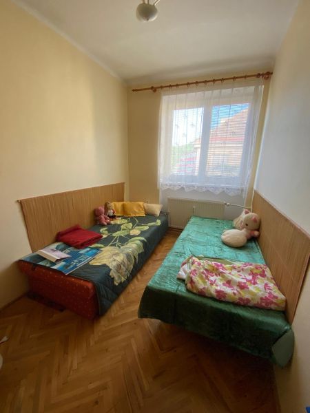 Predaj 3 izbového bytu vo Vyhniach - Izba s dvoma posteľami, drevená podlaha, okno s bielou záclonou v 3-izbovom byte.