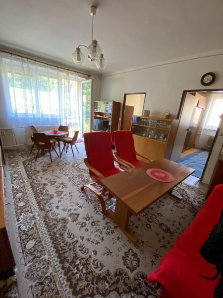 Predaj 3 izbového bytu vo Vyhniach - Obývačka s jedálenským stolom a 3-izbový byt, veľké okno, koberec, staršie zariadenie.