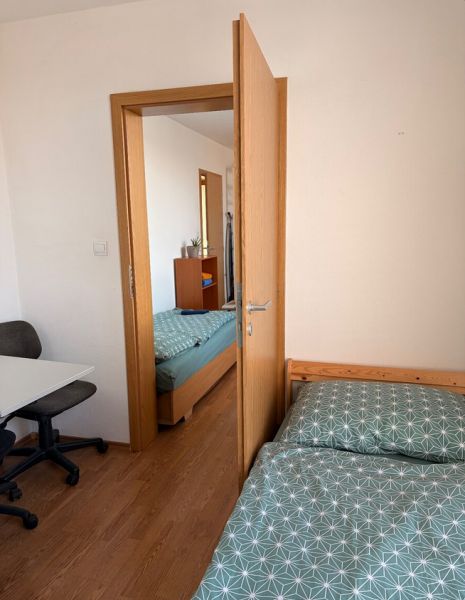 4-izbový byt, Bratislava/Nové Mesto, ulica Nová Rožňavská - Spálňa v 4-izbovom byte s podlahou s dreveným dekorom, posteľou a kancelárskou stoličkou.