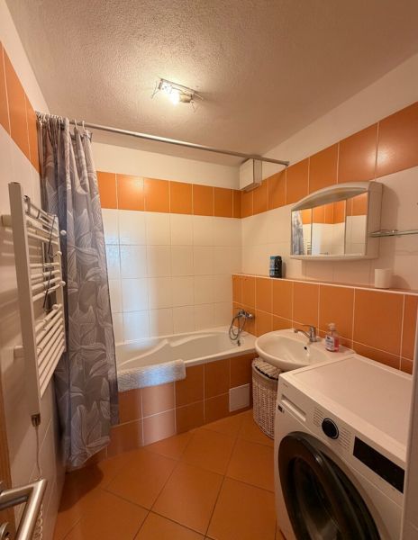 4-izbový byt, Bratislava/Nové Mesto, ulica Nová Rožňavská - Kúpeľňa so sprchovým závesom, práčkou a oranžovými obkladmi v 4-izbovom byte.