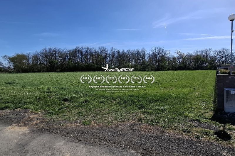 Stavebný pozemok 1212m² v obci Šelpice - Pozemok na bývanie v Šelpiciach na Slnečnej, obklopený trávnatým povrchom a stromami.