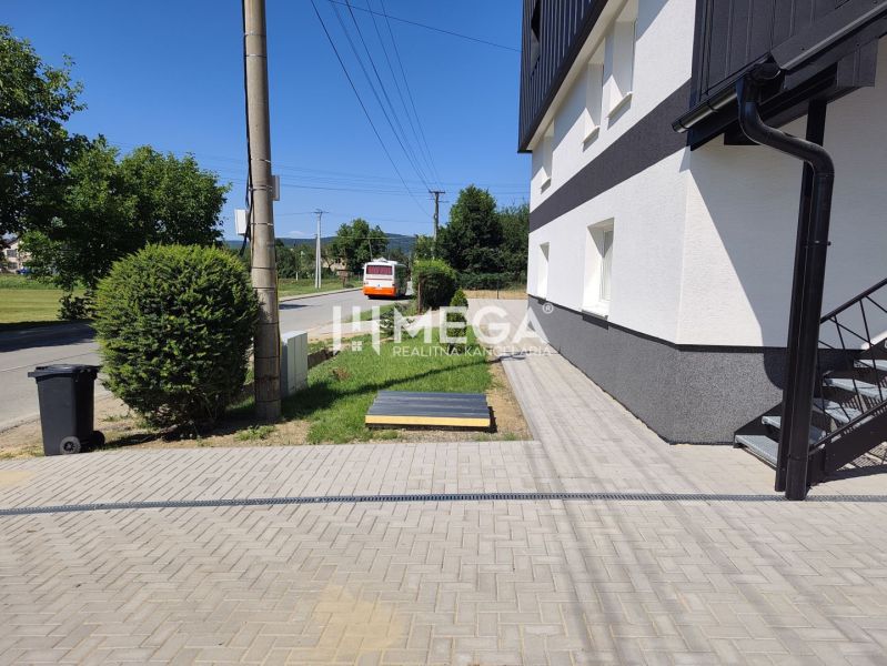 NOVINKA, na predaj tri prémiové 4 izbové byty v obci JASENOV (HE) - Exteriér 4-izbového bytu v Jasenove s cestou a autobusom, obklopený zeleňou.