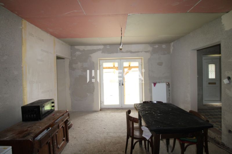 Na predaj - Dom s veľkým pozemkom v Pakostove - Nedokončený interiér s kuchynským stolom, stoličkami a skriňou v rodinnom dome.