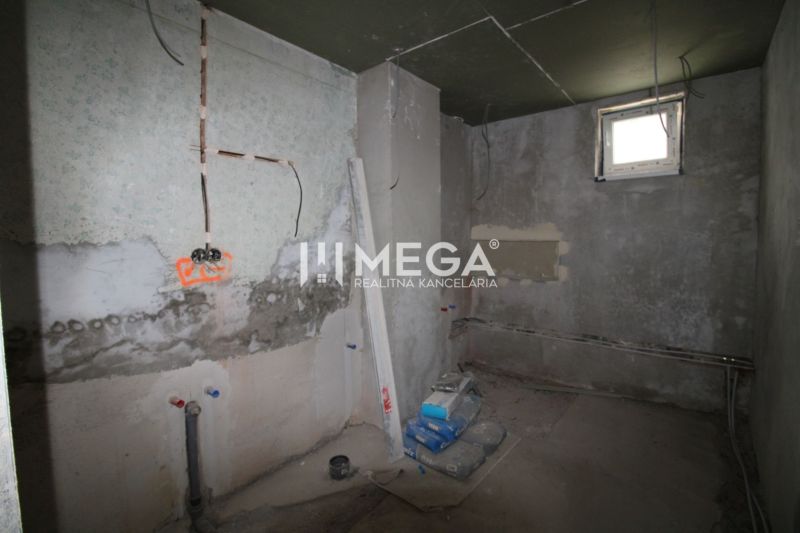 Na predaj - Dom s veľkým pozemkom v Pakostove - Nedokončená miestnosť v rodinnom dome s nedokončenými stenami a stavebným materiálom.