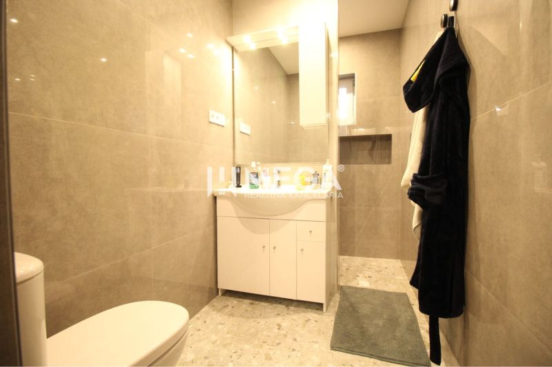 NA PRENÁJOM: Kancelárske priestory + 3-izbový apartmán – Košice - Kúpeľňa s béžovými obkladmi, bielou skrinkou, zrkadlom, vešiakom a zeleným koberčekom.