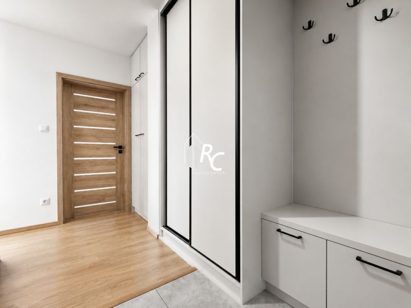 Kompletne zrekonštruovaný 2-izbový byt s 9 m² loggiou Sever - Vstupná chodba so skriňami, vešiakmi a podlahou s dreveným dekorom v 2-izbovom byte.