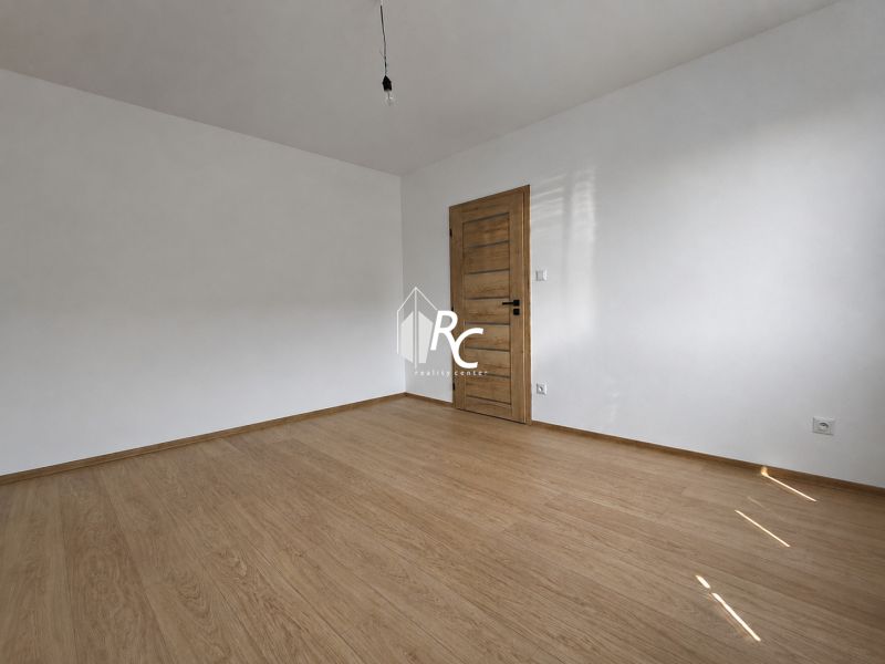 Kompletne zrekonštruovaný 2-izbový byt s 9 m² loggiou Sever - Prázdna izba v 2-izbovom byte s podlahou s dreveným dekorom a drevenými dverami.