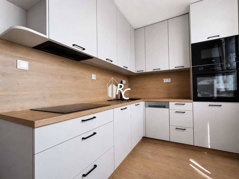 Kompletne zrekonštruovaný 2-izbový byt s 9 m² loggiou Sever - Kuchyňa v 2-izbovom byte s bielymi skrinkami a podlahou s dreveným dekorom.