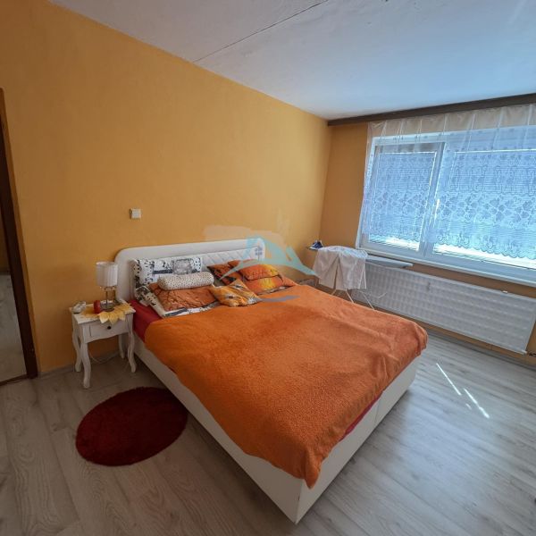 Váš nový štart alebo bezpečná investícia v srdci Šiah - Spálňa s oranžovou stenou, posteľou a podlahou s dreveným dekorom v 2-izbovom byte.