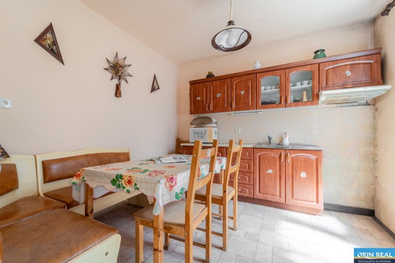 NA PREDAJ RODINNÝ DOM S POZEMKOM O VÝMERE 1003m2 - Kuchyňa v Rodinnom dome so stolom, stoličkami, kuchynskou linkou a dekoračnými prvkami na stene.