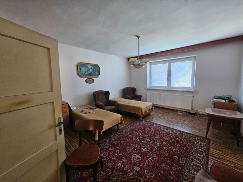 Na predaj rodinný dom s veľkou záhradou v centre V.Šariša - Izba v rodinnom dome so starším nábytkom, podlaha s dreveným dekorom, červený koberec.