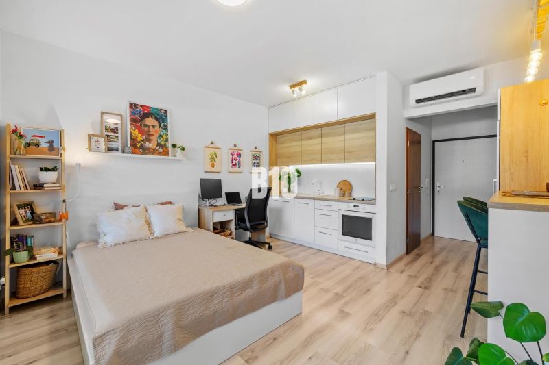 1-IZBOVÝ BYT S VEĽKOU 12 m² TERASOU | SLNEČNICE VILADOMY - 1-izbový byt s podlahou s dreveným dekorom, kuchyňou, posteľou a pracovným stolom.