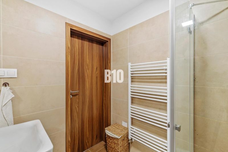 1-IZBOVÝ BYT S VEĽKOU 12 m² TERASOU | SLNEČNICE VILADOMY - Kúpeľňa v 1-izbovom byte s drevenými dverami, sprchovým kútom a radiátorom.