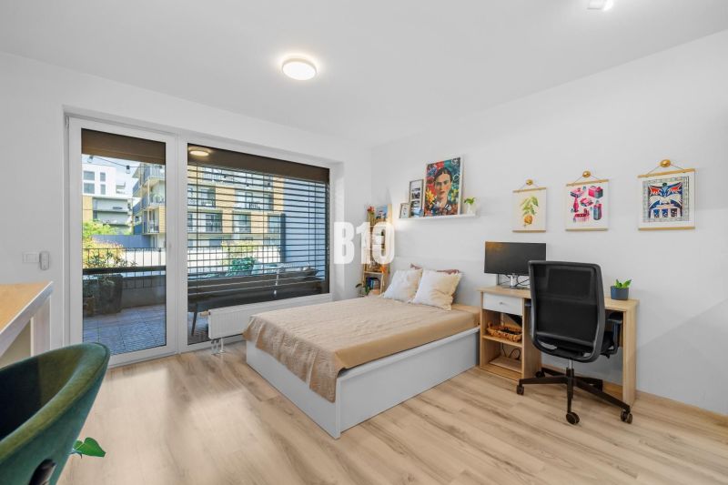 1-IZBOVÝ BYT S VEĽKOU 12 m² TERASOU | SLNEČNICE VILADOMY - 1-izbový byt s podlahou s dreveným dekorom, posteľou a pracovným stolom.