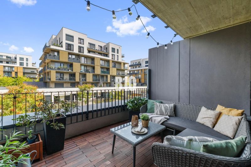 1-IZBOVÝ BYT S VEĽKOU 12 m² TERASOU | SLNEČNICE VILADOMY - Balkón s pohodlným sedením a výhľadom na moderné budovy na Fialovej v Bratislave V.