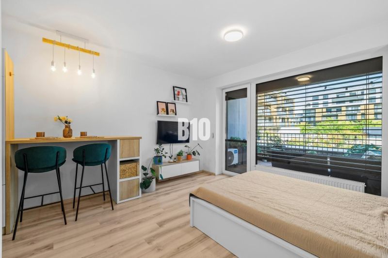 1-IZBOVÝ BYT S VEĽKOU 12 m² TERASOU | SLNEČNICE VILADOMY - 1-izbový byt s podlahou s dreveným dekorom, barový pult a posteľ.