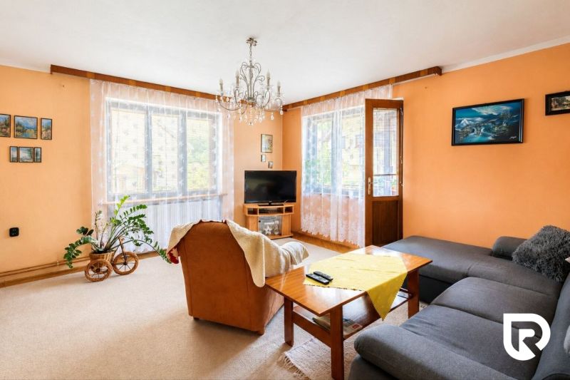 3-IZBOVÝ BYT 90 m² V RODINNOM DOME | POVAŽSKÝ CHLMEC - Žilina - Obývacia izba s krémovými stenami, oranžovým kreslom a šedou sedačkou v rodinnom dome.