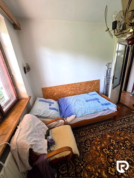 3-IZBOVÝ BYT 90 m² V RODINNOM DOME | POVAŽSKÝ CHLMEC - Žilina - Izba v rodinnom dome so starým kobercom, kreslom a posteľou pri okne.