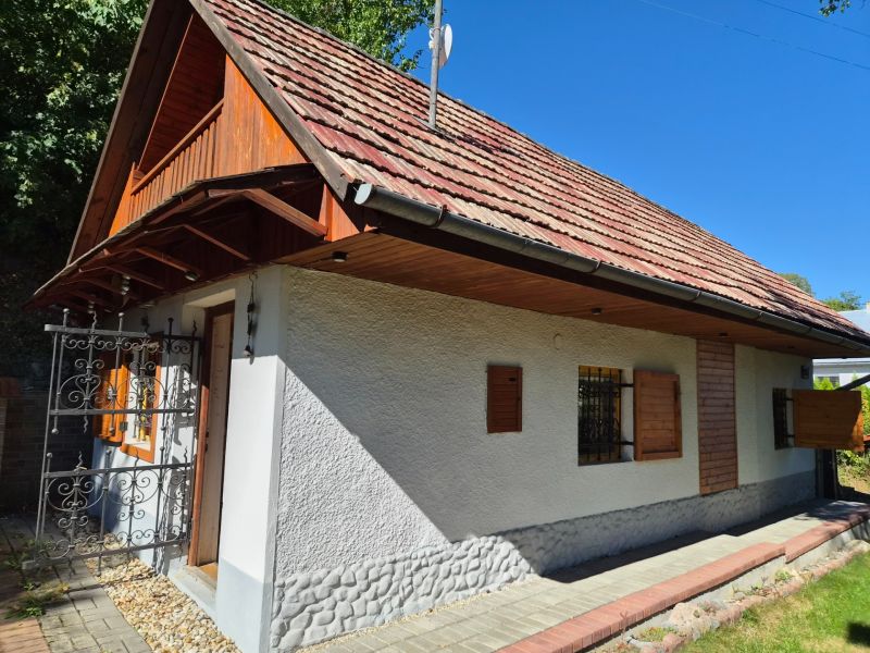 Víkendová chalupa Mikušovce, pozemok 281m2 - Rodinný dom v Mikušovciach s drevenými okenicami a červenou strechou obklopený zeleňou.