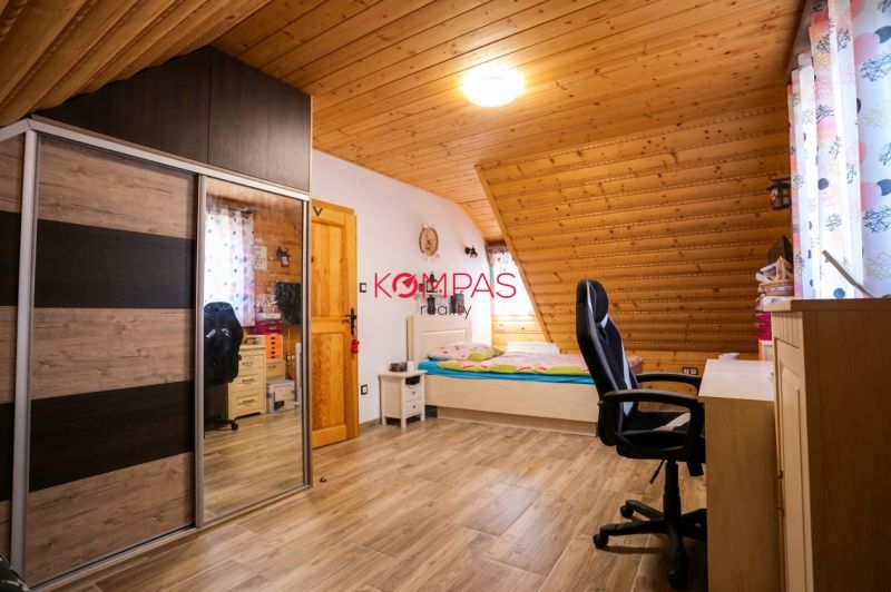 NOVOSTAVBA DOMU V MODERNOM VIDIECKOM ŠTÝLE, OBKLOPENÁ PRÍRODOU A S VEĽ - Podkrovná izba s dreveným obkladom stropu, posteľou, skriňou a podlahou s dreveným dekorom.