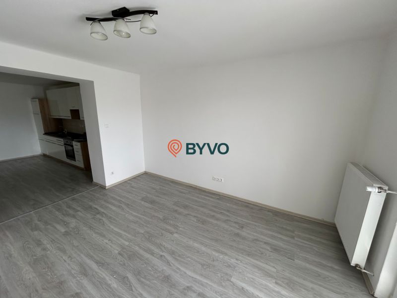3-IZBOVÝ TEHLOVÝ BYT V DUBNICI N/V, BALKÓN, VLASTNÉ KÚRENIE A VÝBORNÉ  - Obývacia izba 3-izbového bytu s podlahou s dreveným dekorom a kuchyňou na ľavej strane.