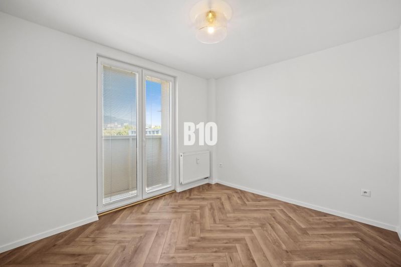 Prémiové bývanie v centre Nitry | 3 izby, veľký balkón - Prázdna izba s podlahou s dreveným dekorom a balkónovými dverami v 3-izbovom byte.