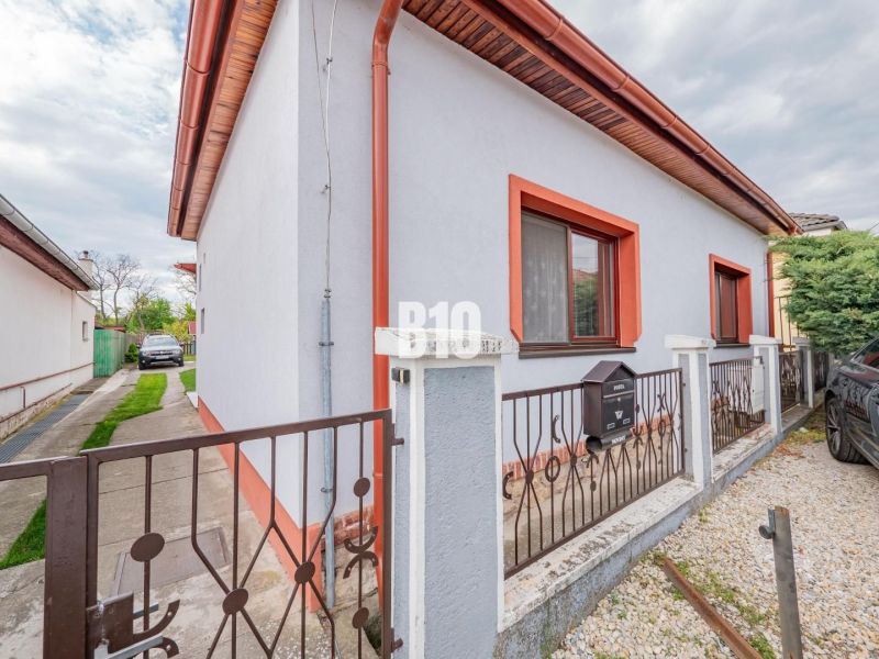Prerobený dom, 981 m2 pozemok - Chrenová, Nitra (TOP lokalita) - Rodinný dom v Nitre s bielou fasádou, červeným lemovaním a záhradkou.