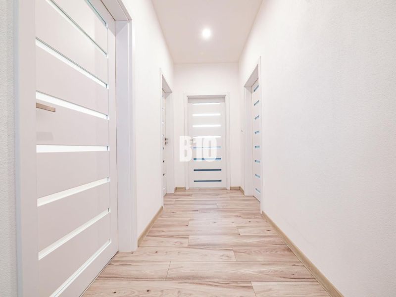 5 izb. bungalov s bazénom, garáž, RED OAK - Nitra, Lužianky - Svetlá chodba v rodinnom dome s podlahou s dreveným dekorom a bielymi dverami.