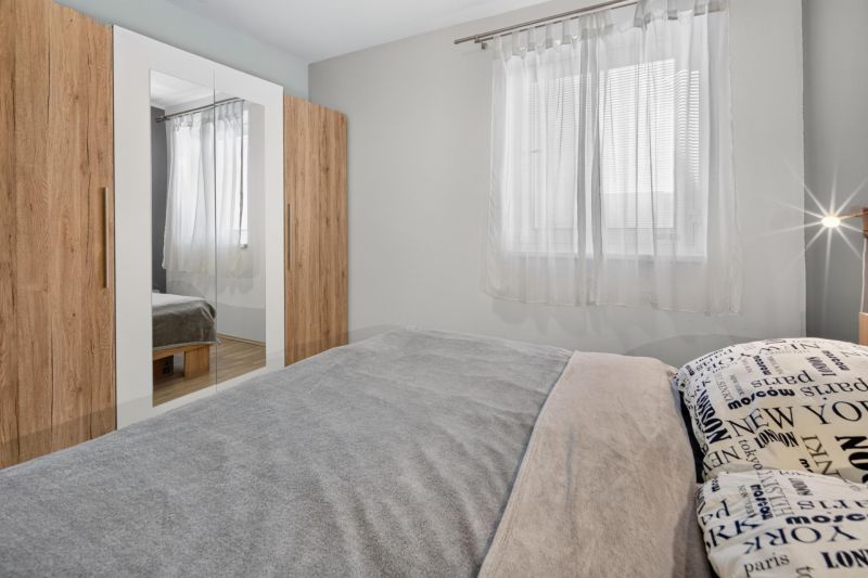 Predaj 2-izbový byt GREEN VILLAGE, loggia, parkovanie, Dunajská Lužná - Spálňa v 2-izbovom byte s posteľou, skriňou a bielymi závesmi na okne.