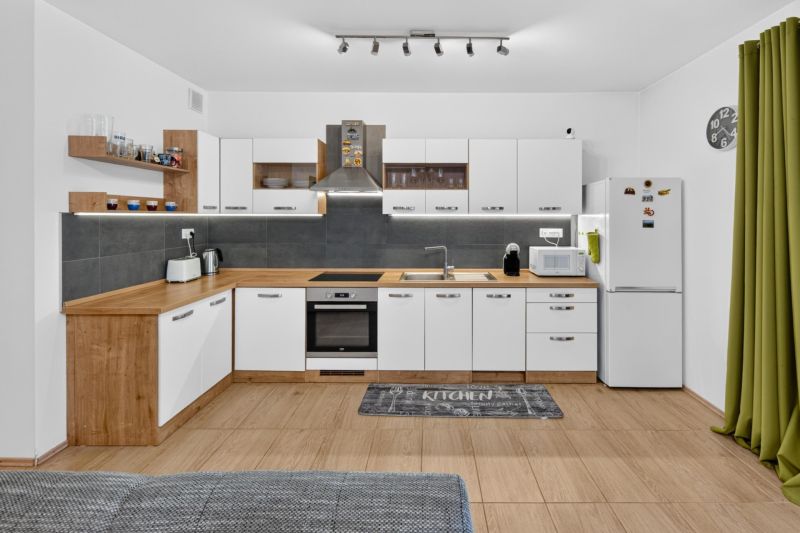 Predaj 2-izbový byt GREEN VILLAGE, loggia, parkovanie, Dunajská Lužná - Kuchyňa v 2-izbovom byte s bielym nábytkom, sivými obkladmi, podlahou s dreveným dekorom.