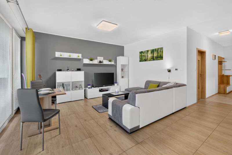 Predaj 2-izbový byt GREEN VILLAGE, loggia, parkovanie, Dunajská Lužná - Obývacia izba v 2-izbovom byte s pohovkou, televízorom a podlahou s dreveným dekorom.