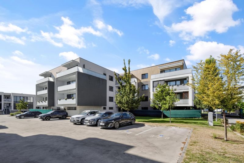 Predaj 2-izbový byt GREEN VILLAGE, loggia, parkovanie, Dunajská Lužná - Bytové domy na Orechovej ulici v Dunajskej Lužnej so zaparkovanými autami a zeleňou.
