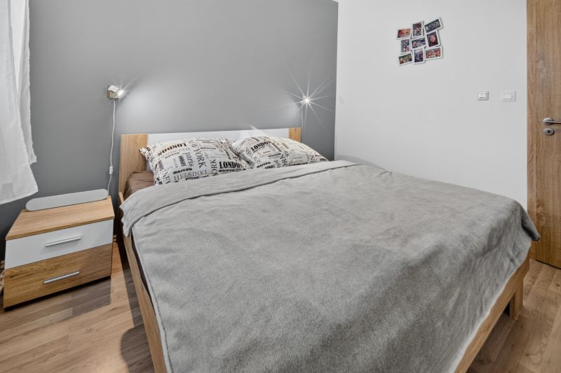 Predaj 2-izbový byt GREEN VILLAGE, loggia, parkovanie, Dunajská Lužná - Spálňa s posteľou a nočným stolíkom, 2-izbový byt, podlaha s dreveným dekorom.