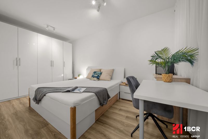 1.BCR | PRIESTRANNÝ 2-IZB. APARTMÁN V MAMAPAPA, PIVNICA, PARKING - Svetlá spálňa s bielym nábytkom, písací stôl a podlaha s dreveným dekorom, 2-izbový byt.