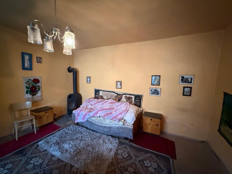 DOM NA PRENÁJOM, Obec Sikenica, okres Levice - Spálňa v rodinnom dome s kachľami, posteľou a ozdobnými obrázkami na stene.