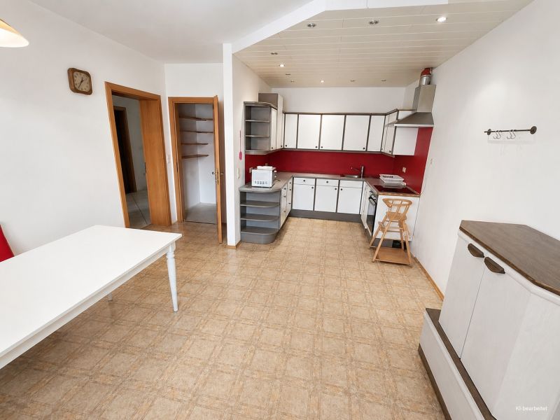 Predaj rodinného domu, Neusiedl am See - Kuchyňa v rodinnom dome s červenými akcentmi a podlahou s dreveným dekorom.