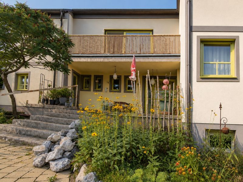 Predaj rodinného domu, Neusiedl am See - Rodinný dom v Podersdorf am See s kamennými schodmi a záhradou plnou kvetín.
