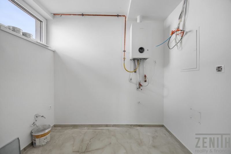 Moderný rodinný dom, ktorý vás prekvapí priestorom aj atmosférou - Biela miestnosť s bojlerom a podlahou s dreveným dekorom v rodinnom dome.